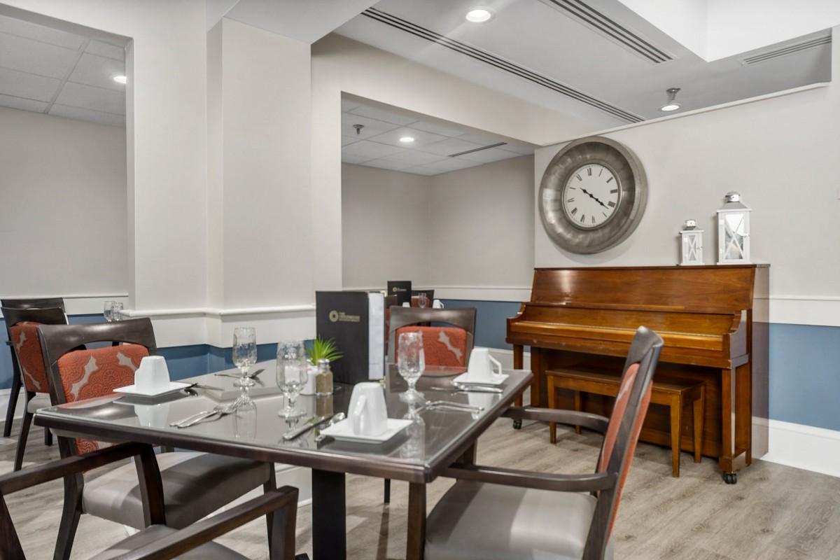 An elegant dining area with a neatly set table, a piano, and a large decorative clock on the wall.