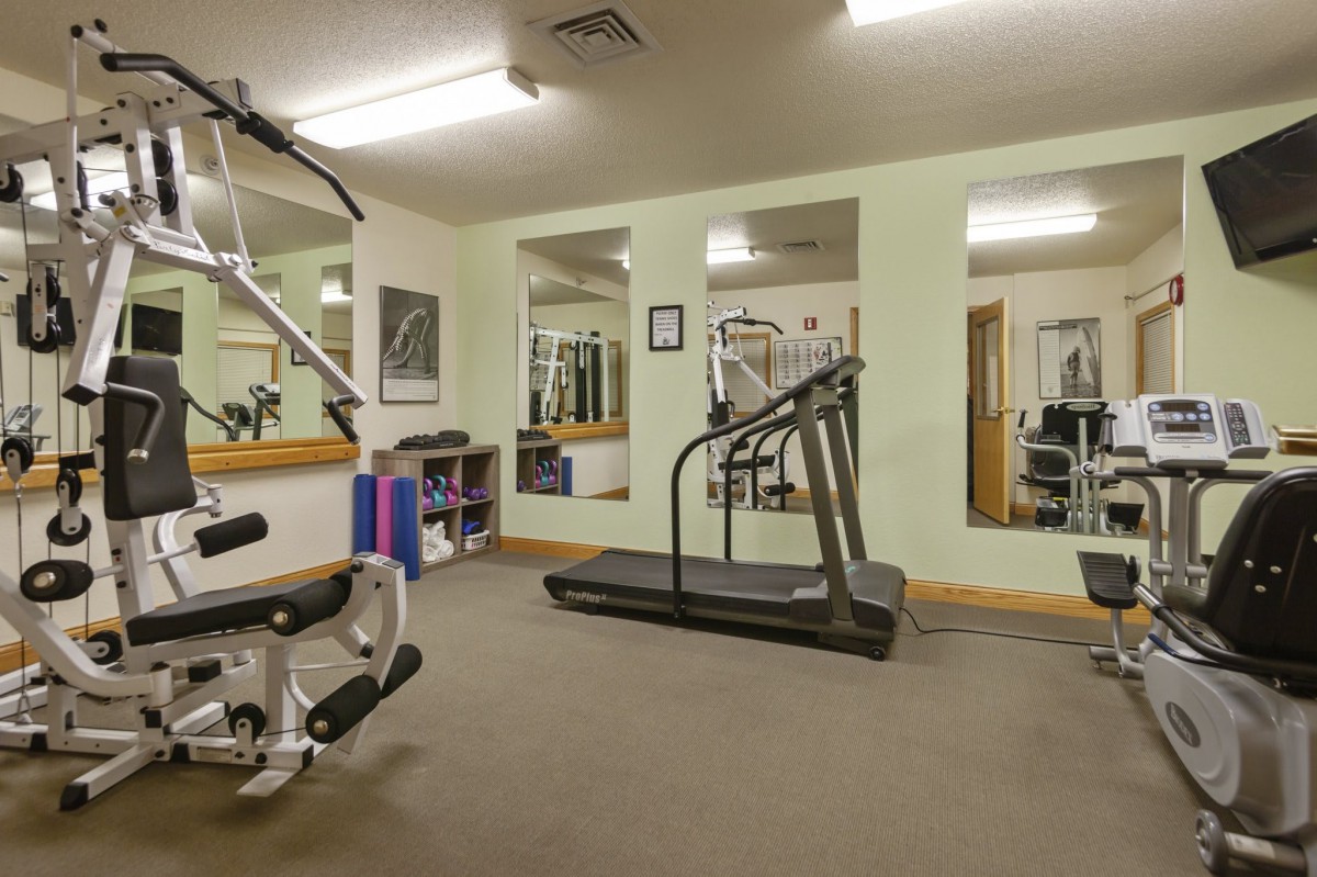 A small gym with exercise equipment including a treadmill, weights, and mirrors.