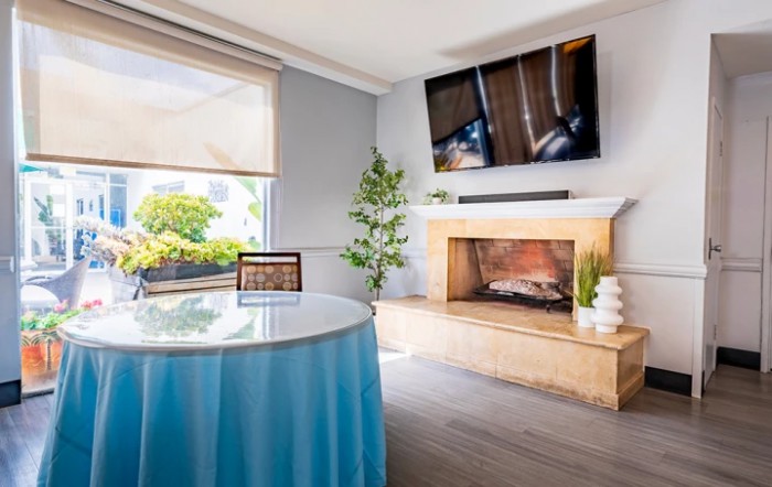 A modern living room featuring a fireplace, wall-mounted television, and a table draped with blue cloth.