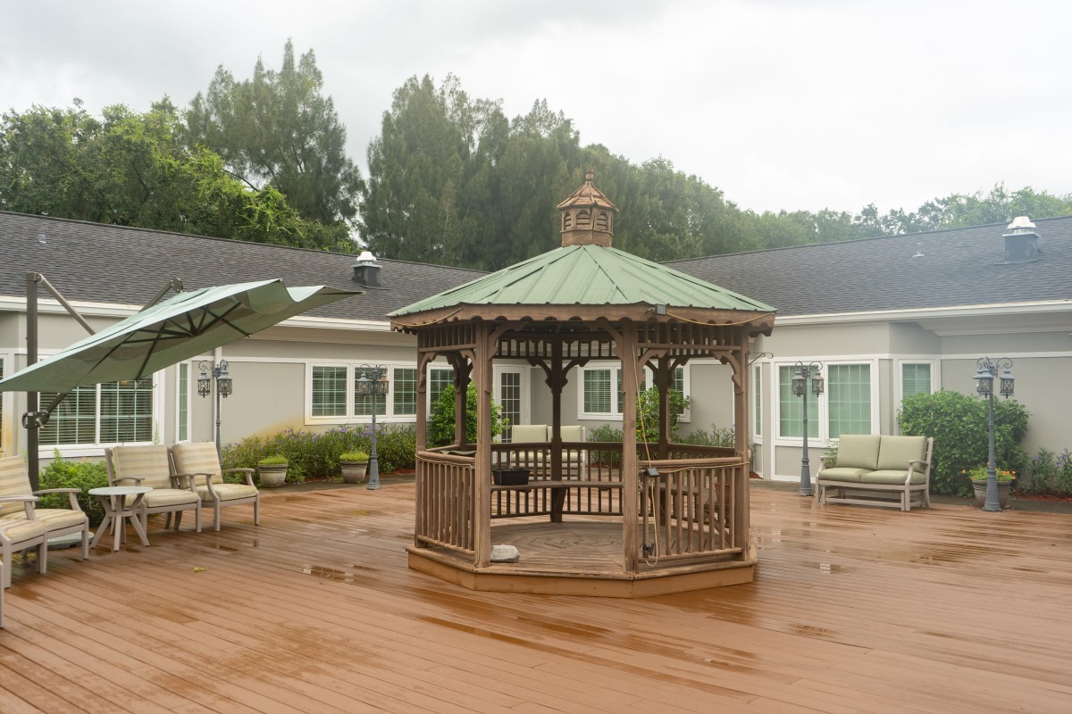 A wooden gazebo on an outdoor deck surrounded by patio furniture.