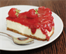 A slice of strawberry cheesecake served on a white plate with a spoon.