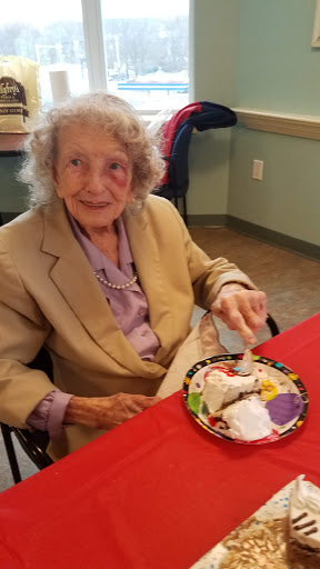 An elderly woman enjoying a dessert at a communal dining setting.