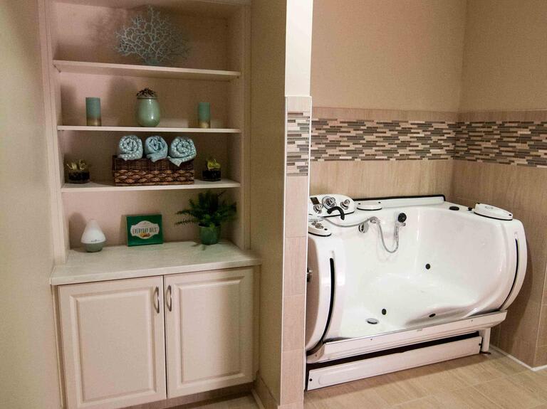 A bathroom with a built-in bathtub and neatly organized shelves with towels and decor.