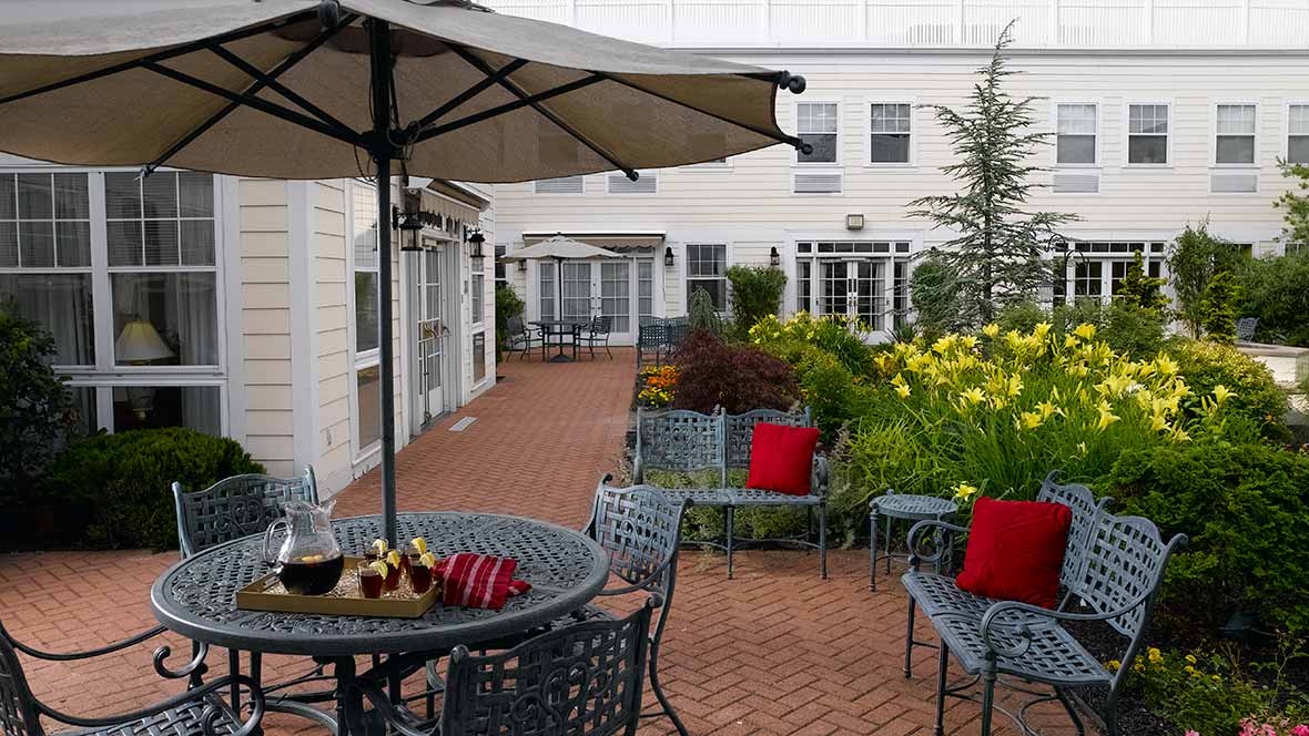 A cozy patio with outdoor seating and umbrellas, surrounded by a lush garden.