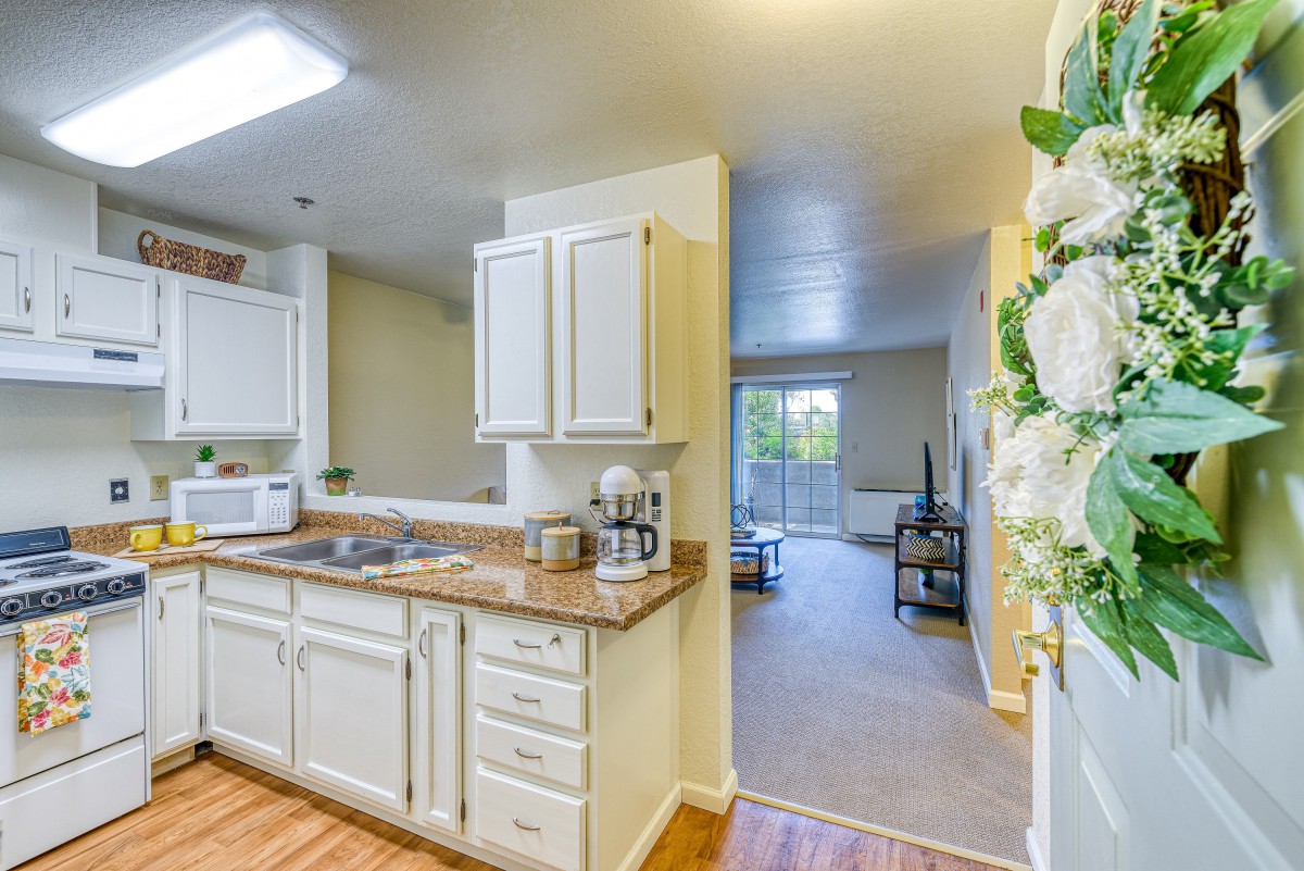 A cozy kitchen with white cabinets leading into a bright living room.