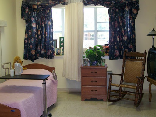 A cozy hospital room featuring a bed, a rocking chair, and a small plant beside the window.