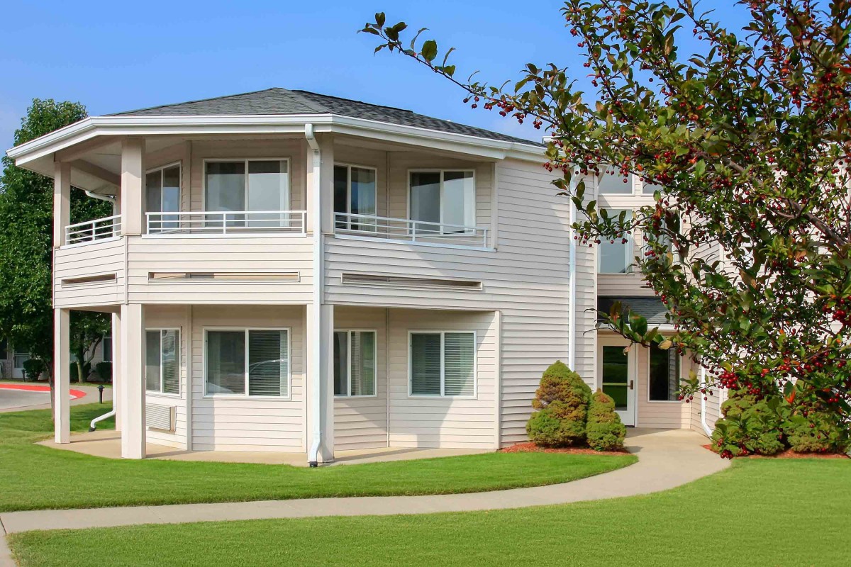 A modern residential building with a well-maintained lawn and surrounding greenery.