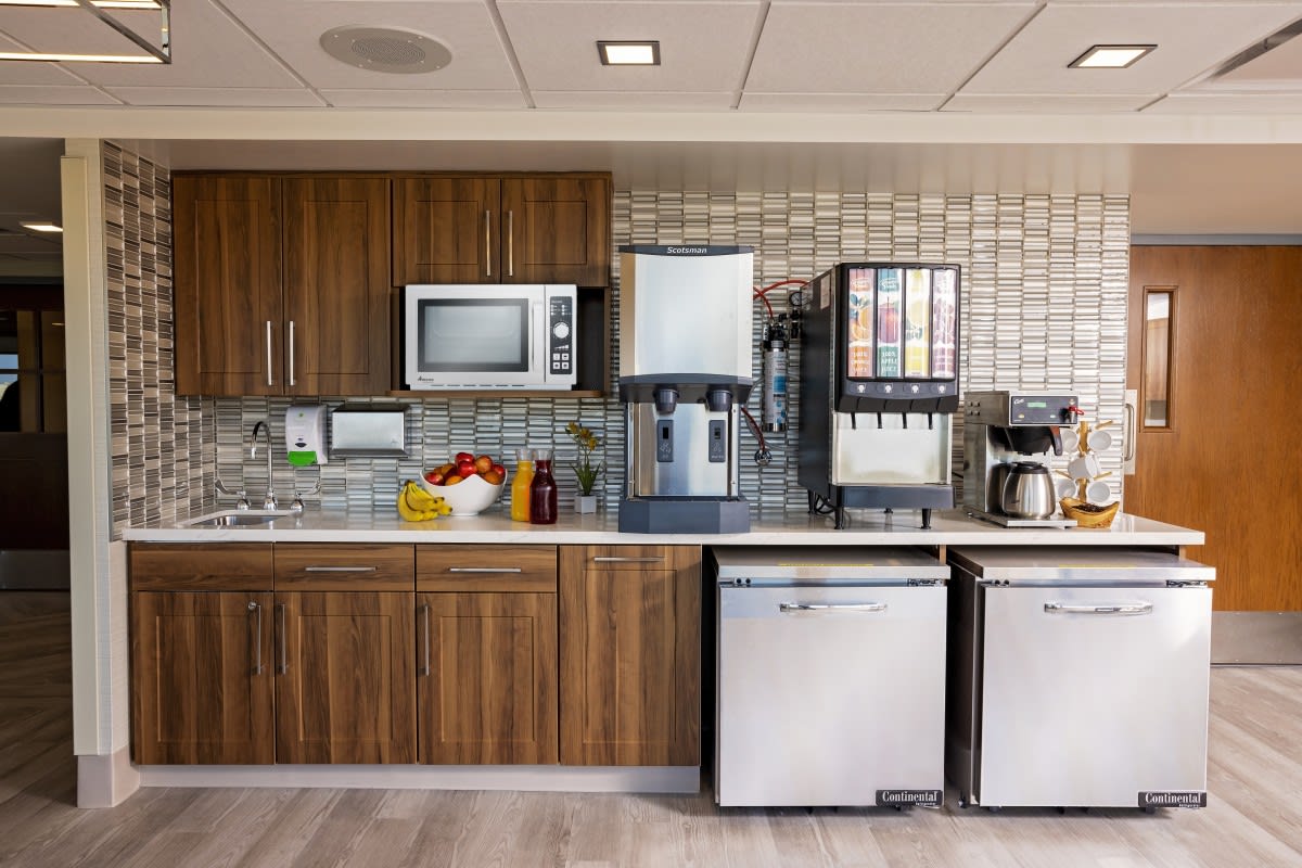 An office kitchen area with various appliances including a microwave, coffee maker, and drink dispenser.
