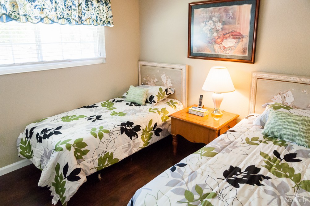 A cozy bedroom with twin beds and floral bedding, featuring a nightstand with a lamp and wall art above.