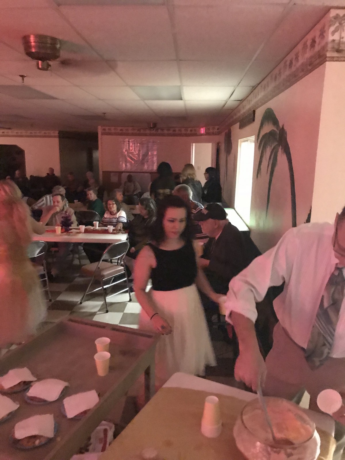 A group of people socializing at an indoor event with tables set up.