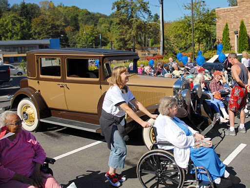 A lively community parade featuring a vintage car and participants in wheelchairs enjoying the festivities.
