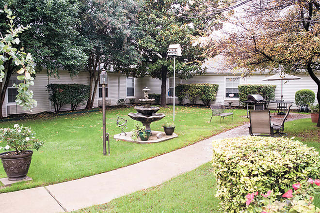 A serene garden with a central fountain, surrounded by lush greenery and benches, providing a peaceful outdoor environment.