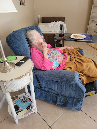 An elderly woman enjoys a moment of relaxation in her favorite chair, snacking and unwinding at home.