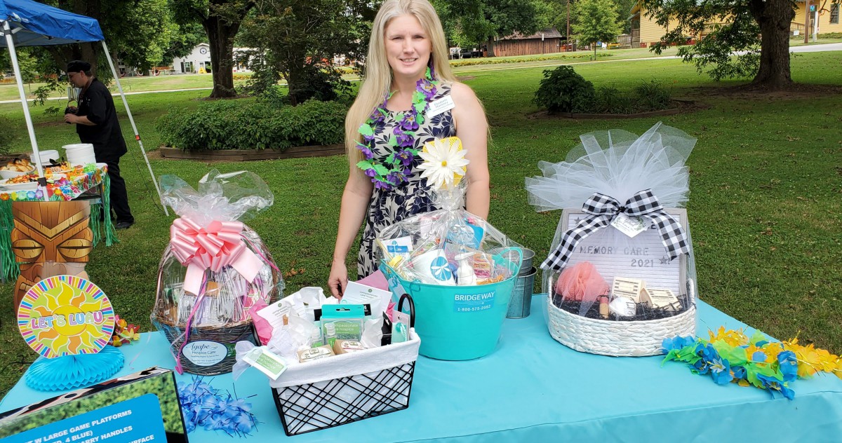 A woman stands behind a table with beautifully arranged gift baskets at an outdoor event.