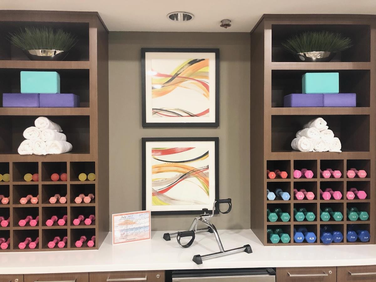 A well-organized exercise room with colorful dumbbells, neatly folded towels, yoga blocks, and abstract artwork on the wall.
