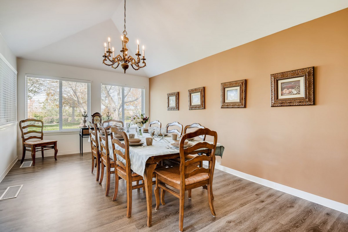 A cozy dining room with a long wooden table, chairs, and a chandelier overhead, accented by framed artwork on the walls.