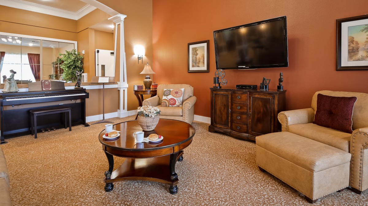 A cozy living room with a warm color scheme, featuring a sofa, armchairs, a wooden coffee table, and a mounted flat-screen TV.