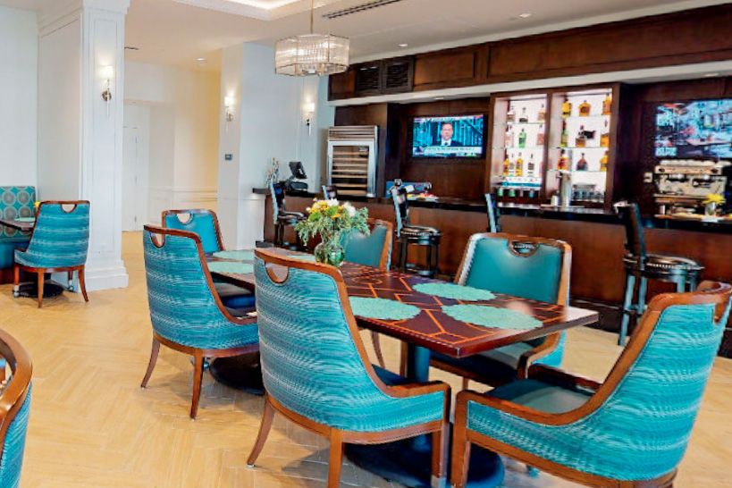 A modern lounge area with a bar, featuring teal upholstered seating and a mounted television.