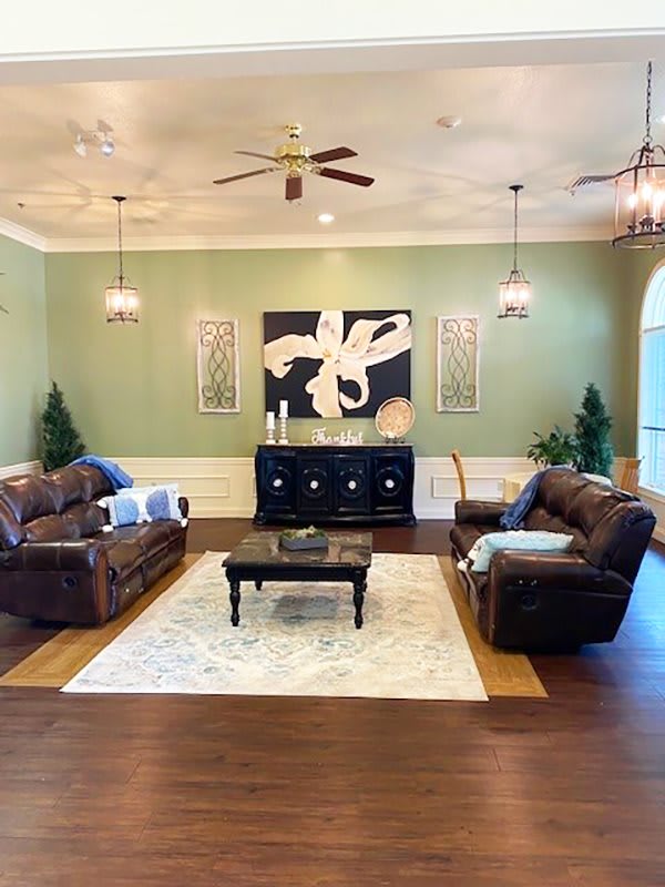 A well-decorated living room featuring leather sofas, a central coffee table, and wall art, all framed within a warm color palette and elegant lighting.