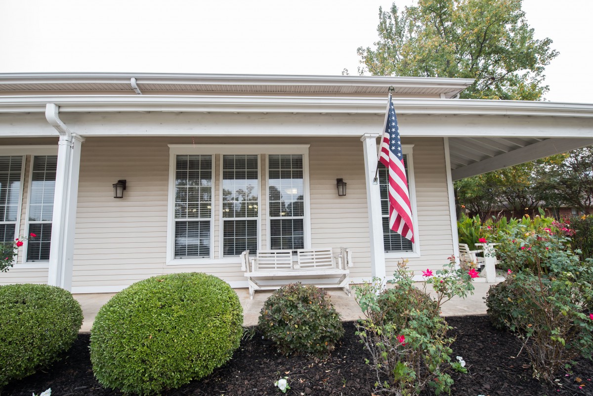 A house with a front porch, displaying an American flag and surrounded by greenery.