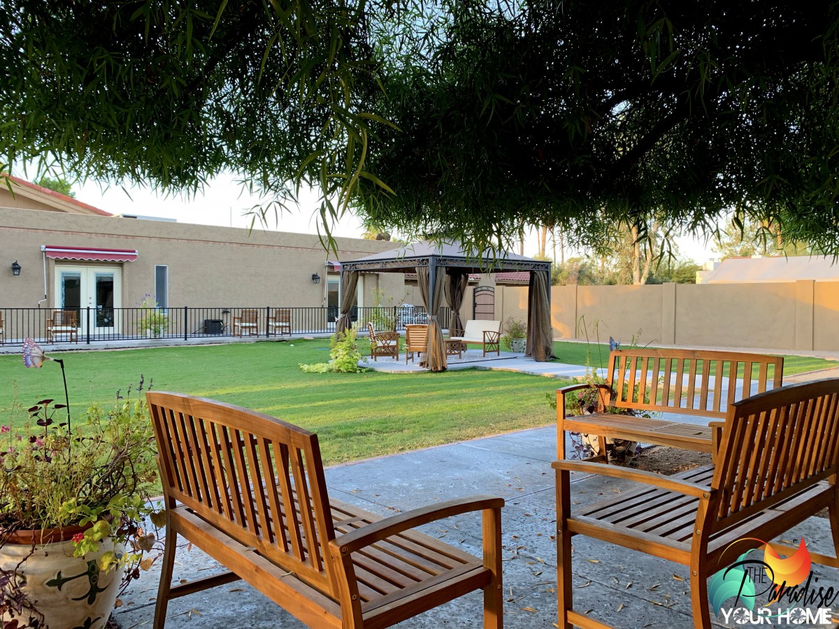 A peaceful garden scene with wooden benches, a green lawn, and a gazebo in the background.