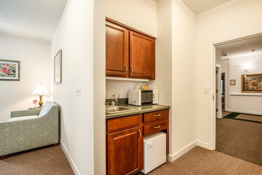 A compact kitchenette with wooden cabinets, a sink, a microwave, and a mini fridge.