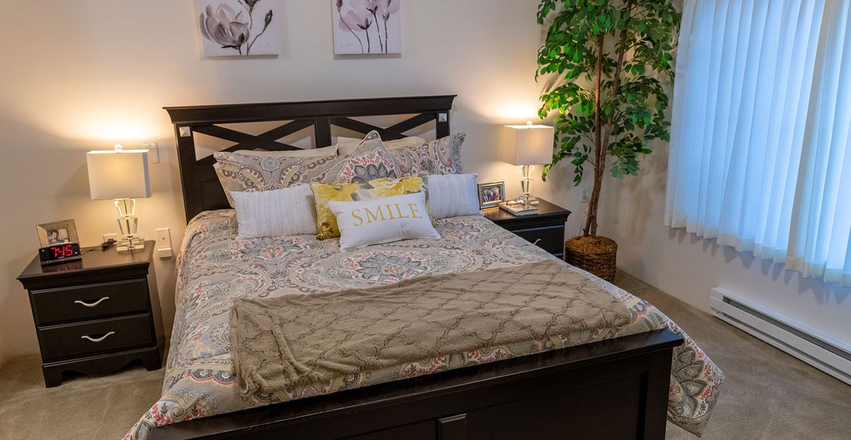 A cozy and well-decorated bedroom with a neatly made bed, featuring multiple pillows and a warm blanket, accompanied by stylish bedside lamps and an indoor plant.