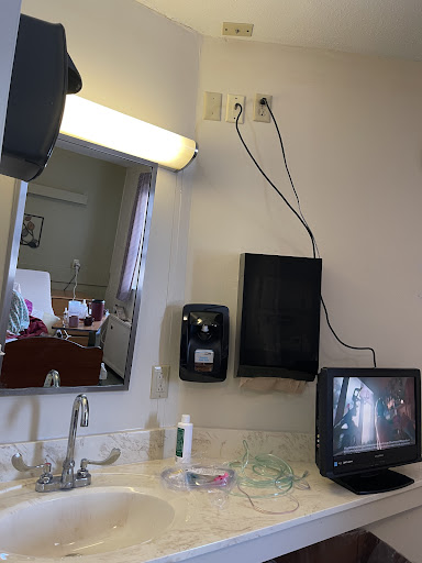A room featuring a sink area with a mirror, television, and various hygiene products.