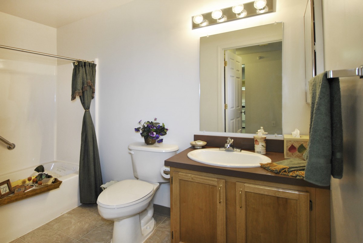 A modern bathroom featuring a sink with a wooden cabinet, a toilet, and a shower with a curtain, illuminated by overhead lighting.