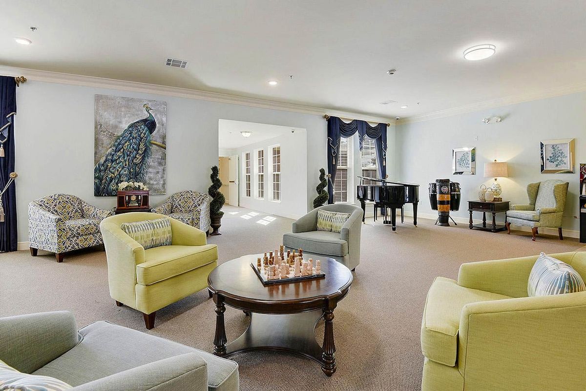 A spacious and elegantly decorated living room featuring comfortable seating, a piano, artwork, and a chessboard on the table.