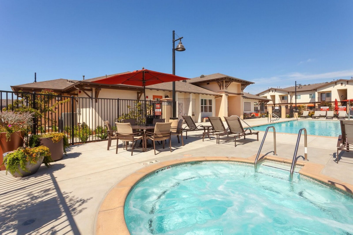 A sunny outdoor area featuring a swimming pool surrounded by patio furniture and umbrellas, providing a relaxing resort atmosphere.
