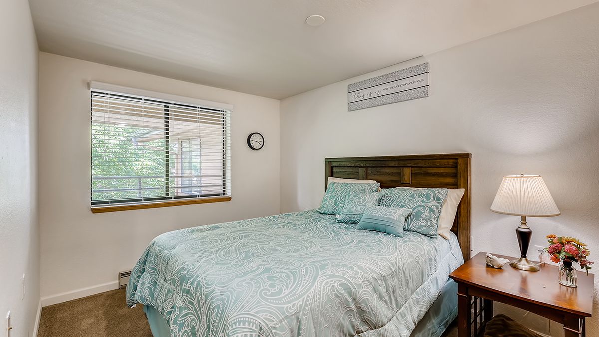 A cozy bedroom featuring a neatly made bed with blue bedding, a wooden headboard, and a window with blinds.