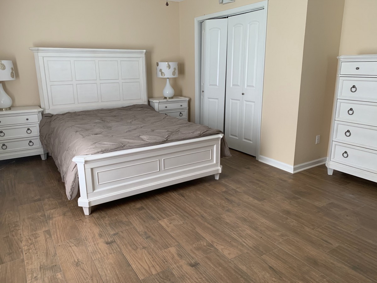 A neatly arranged bedroom with a bed, nightstand, and closet on a wooden floor.