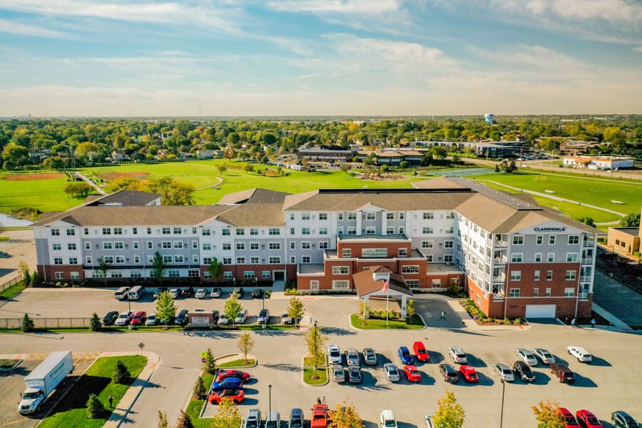 Aerial view of a large residential building with a parking lot and surrounding suburban landscape.