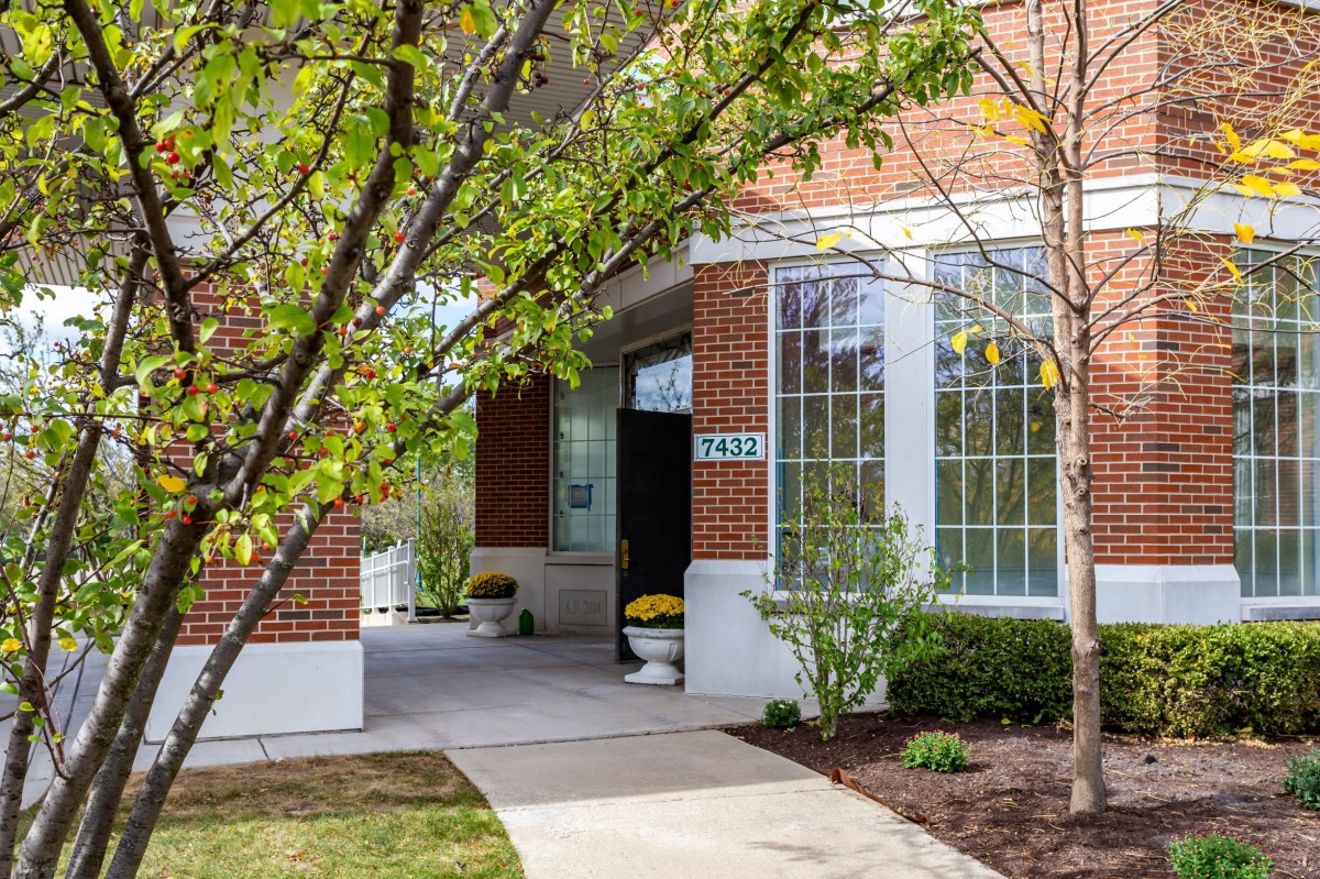 A brick building entrance with large windows and surrounding greenery.