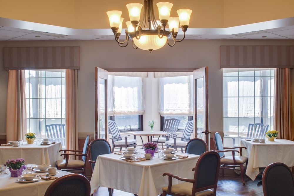 A cozy dining room with a chandelier, set for a meal near large windows.