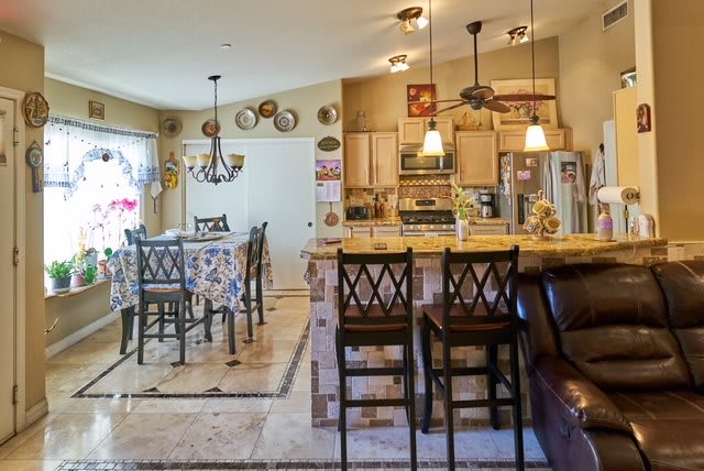 A modern kitchen and dining area with bar stools, chandeliers, and decorative plates on the wall.