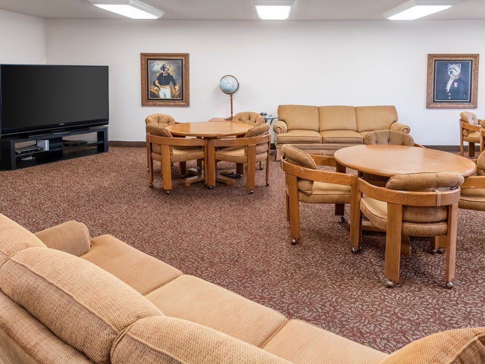 A cozy living room with beige sofas, round tables, wooden chairs, and a television.