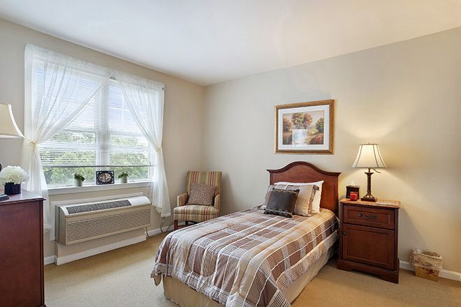 A cozy bedroom with a single bed, armchair, and a nightstand beside a lamp.
