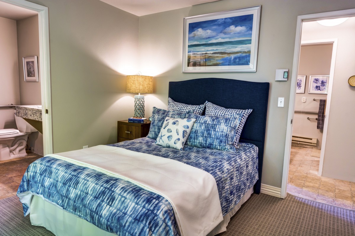 A cozy bedroom with blue-themed bedding and a framed landscape painting above the bed.
