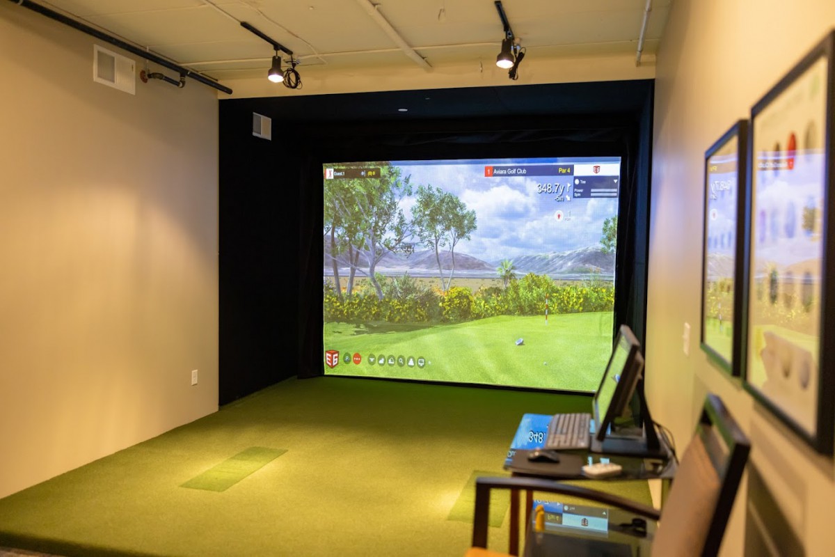 An indoor golf simulator setup featuring a virtual golf course displayed on a large screen.