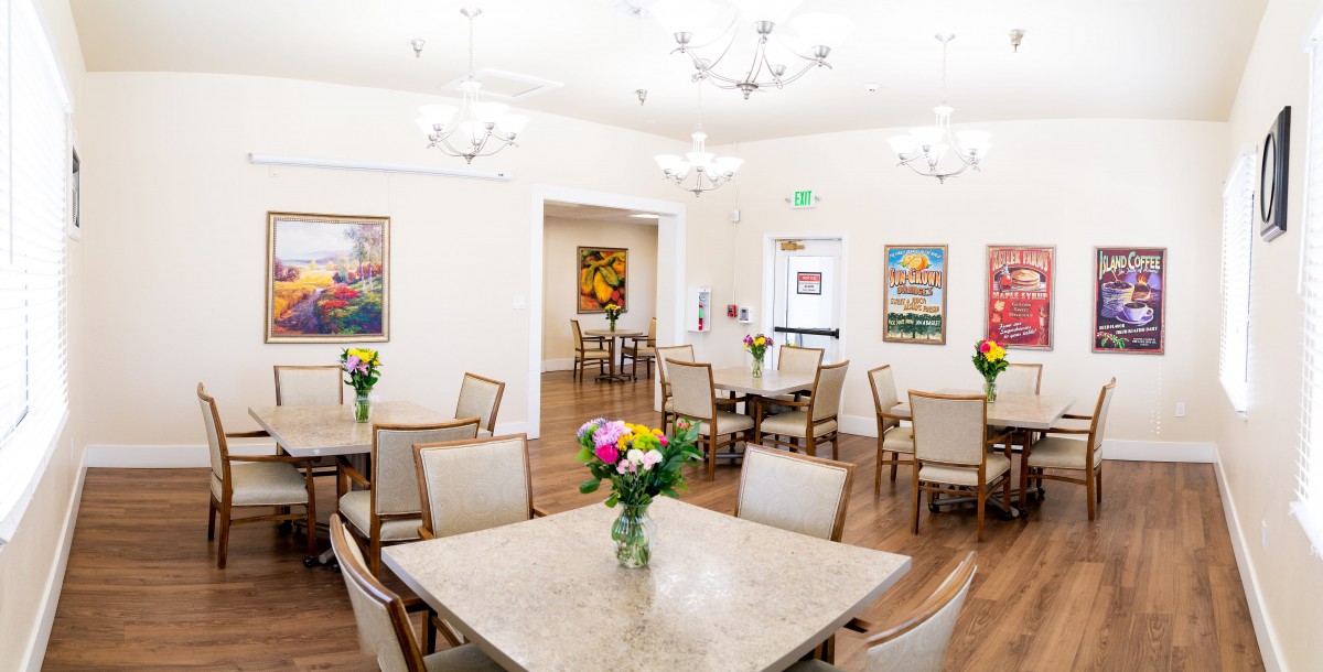 A bright and inviting dining room with elegantly arranged tables, chairs, and floral centerpieces under modern chandeliers.