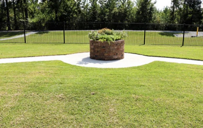 A circular brick planter in the middle of a grassy garden area, surrounded by a fence.