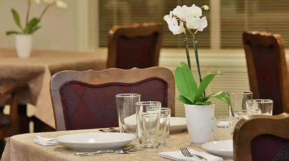 A dining table elegantly set with plates, glasses, and a white orchid centerpiece.