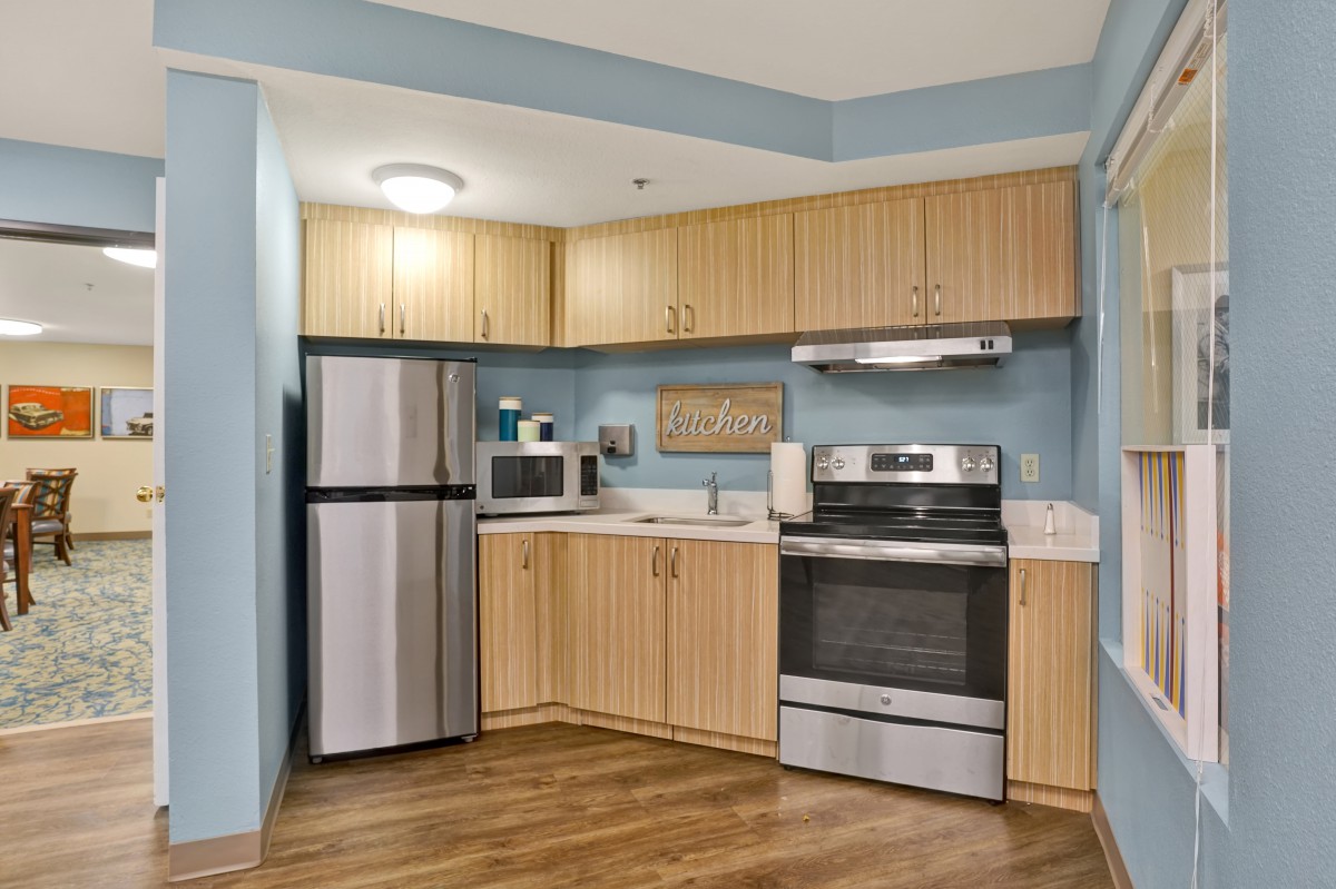 A modern kitchen with wood cabinets, featuring a refrigerator, oven, and microwave.