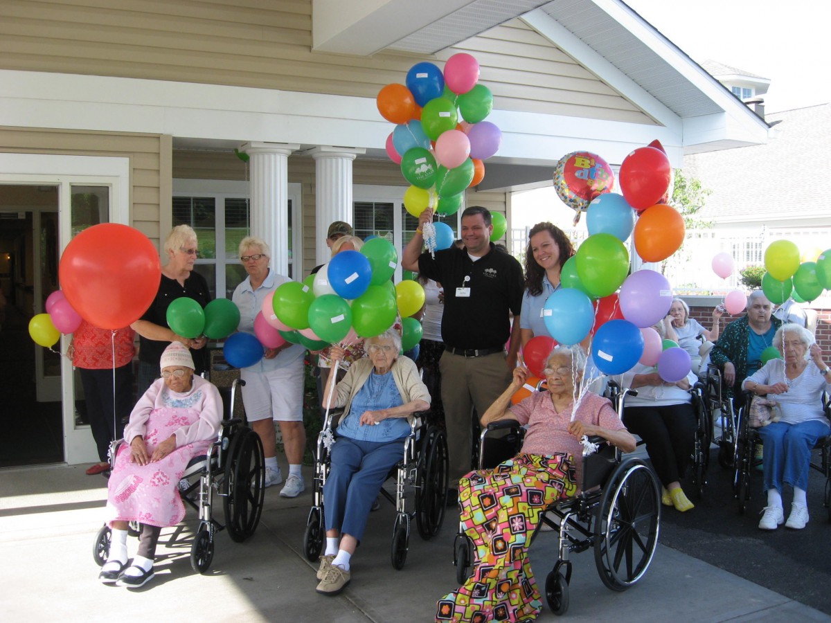 A joyful group of elderly individuals celebrating outdoors with colorful balloons, some in wheelchairs.