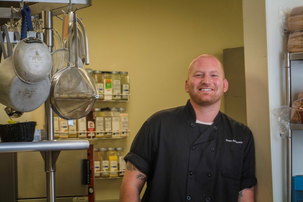 A chef smiling in a professional kitchen setting.