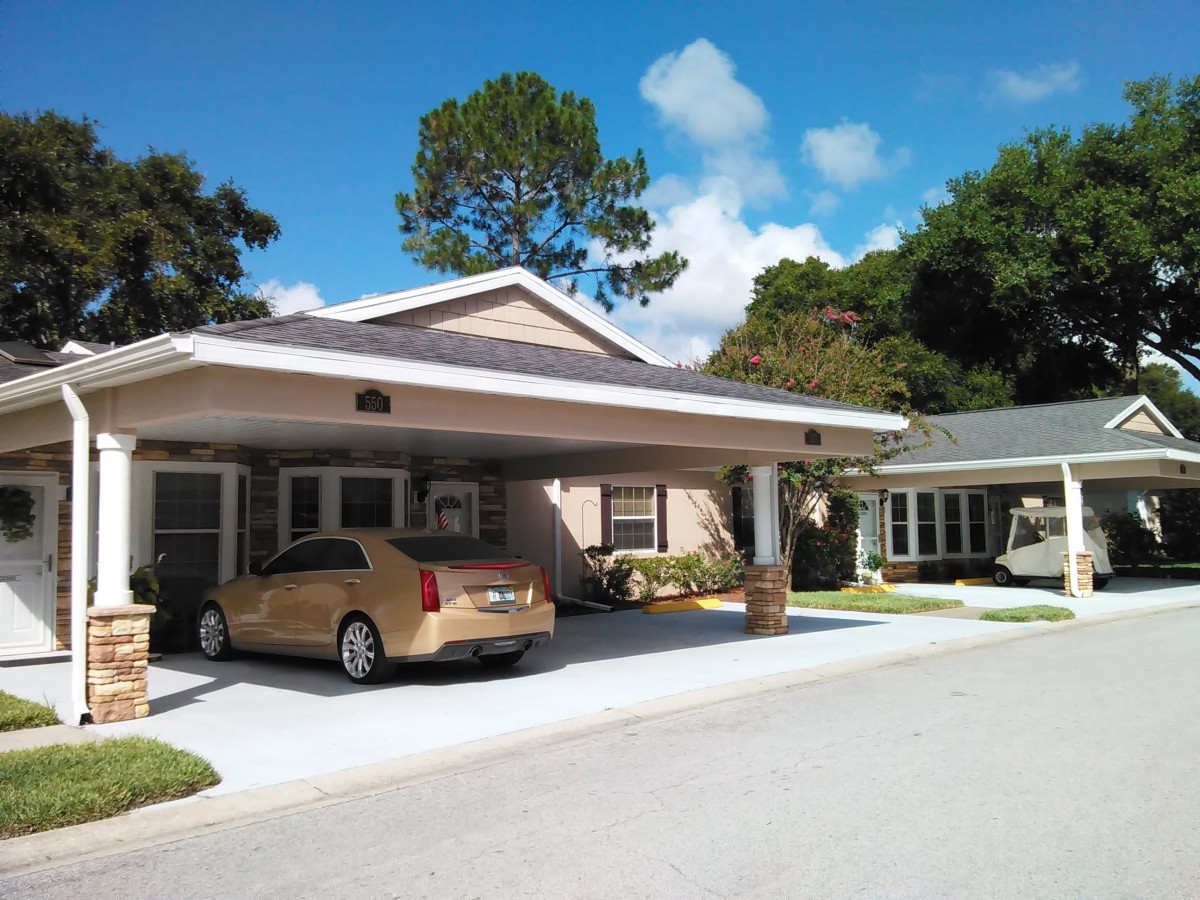 A suburban house with a car parked in the driveway, surrounded by trees and a clear blue sky.