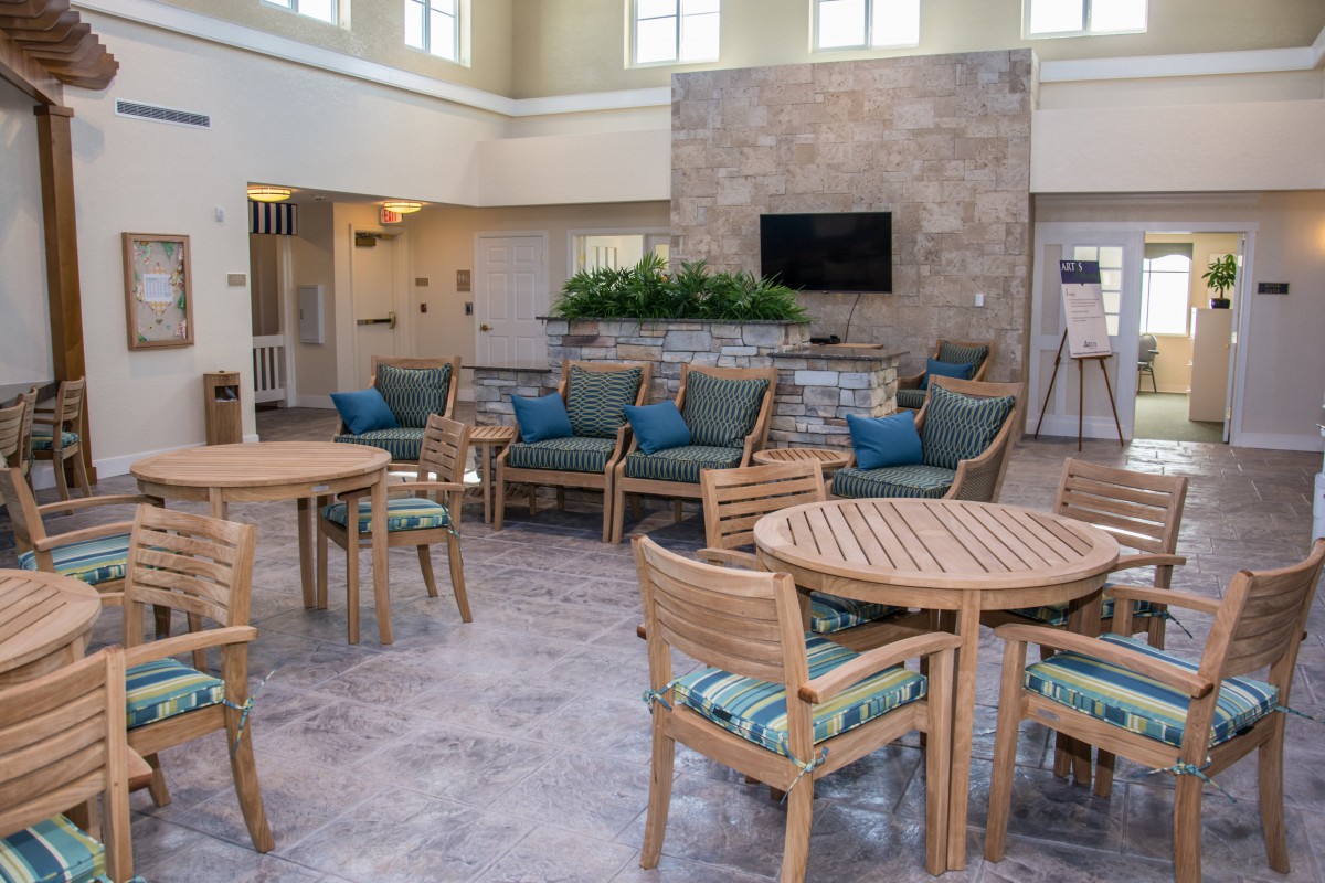 A modern lounge area with wooden tables and chairs, featuring comfortable seating and a television on the wall.