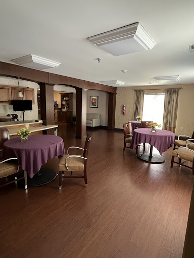 A spacious dining area featuring round tables with purple tablecloths and comfortable seating, illuminated by natural light.